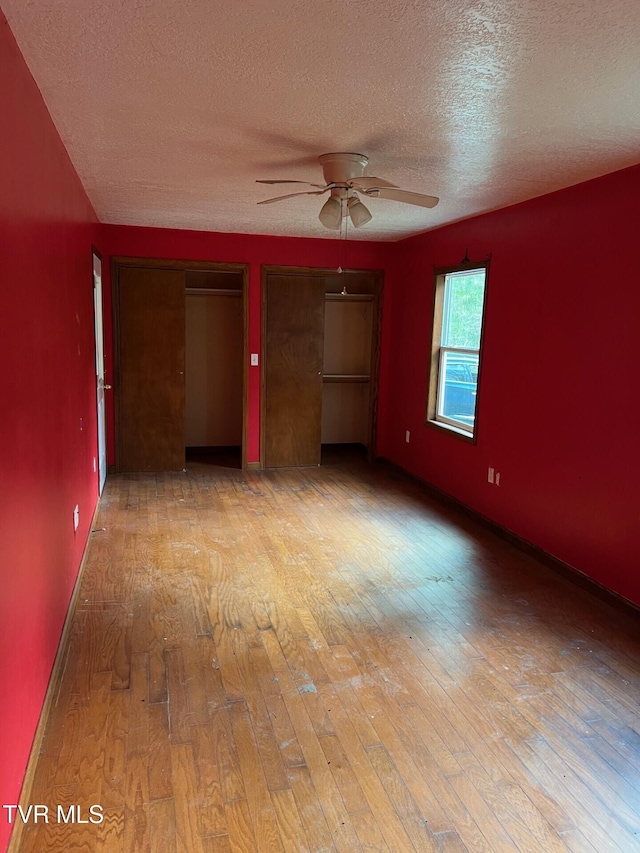 unfurnished bedroom with light hardwood / wood-style floors, ceiling fan, a textured ceiling, and two closets