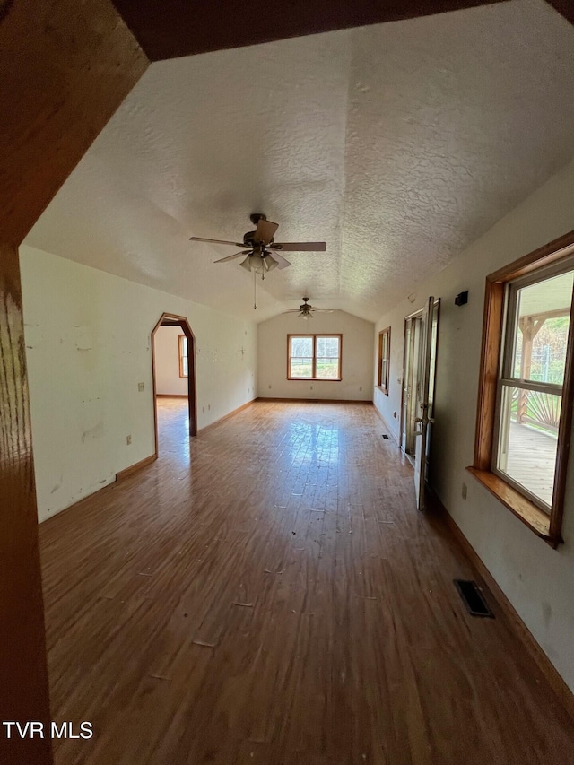 unfurnished living room with ceiling fan, dark hardwood / wood-style floors, a textured ceiling, and vaulted ceiling