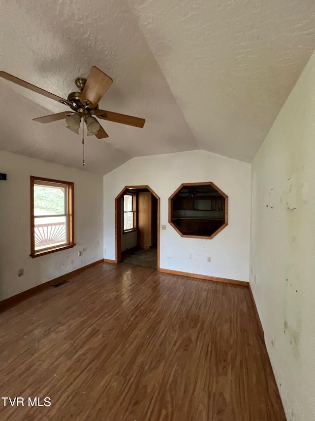 unfurnished living room with dark wood-type flooring, a textured ceiling, ceiling fan, and vaulted ceiling