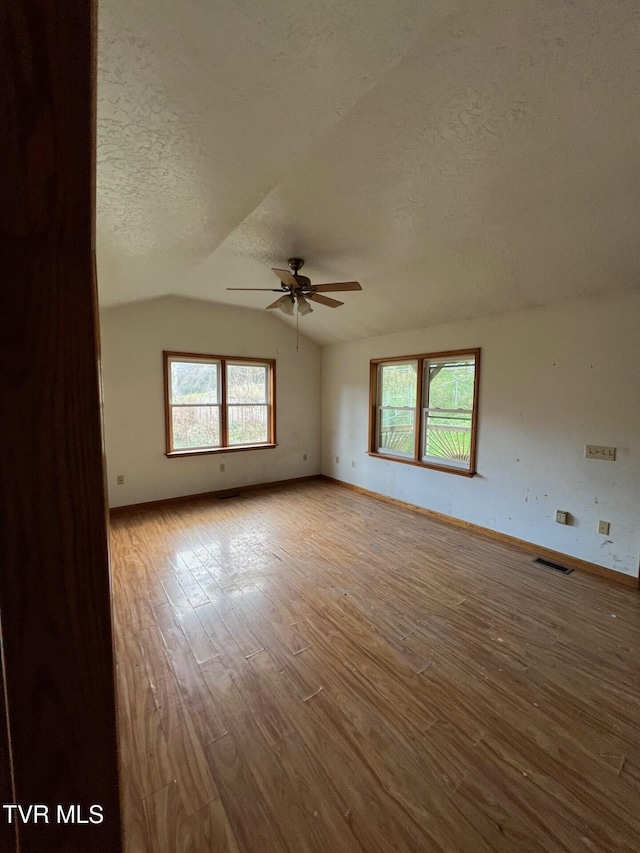 unfurnished room with ceiling fan, a textured ceiling, light wood-type flooring, and vaulted ceiling