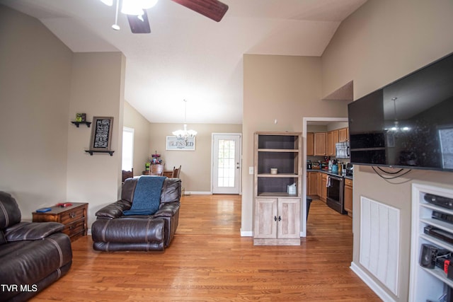 living room featuring ceiling fan with notable chandelier, light hardwood / wood-style floors, and vaulted ceiling