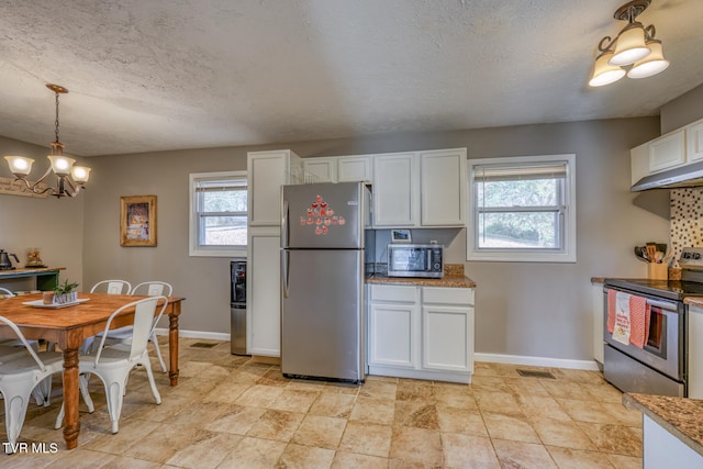 kitchen featuring a textured ceiling, stainless steel appliances, white cabinetry, baseboards, and hanging light fixtures