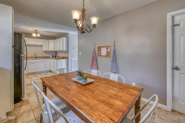 dining space featuring a textured ceiling, baseboards, visible vents, and an inviting chandelier