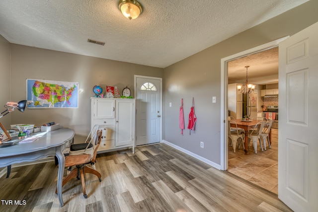 office space featuring a chandelier, a textured ceiling, wood finished floors, visible vents, and baseboards