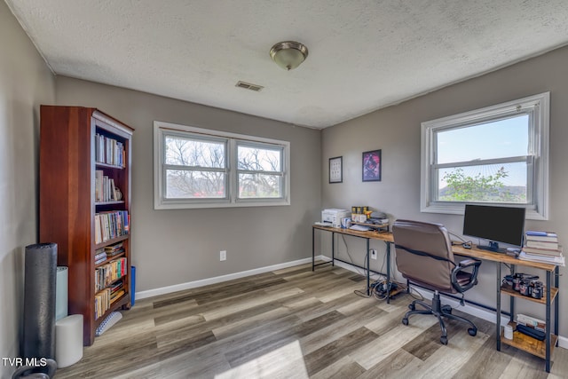 home office featuring a healthy amount of sunlight, a textured ceiling, visible vents, and wood finished floors