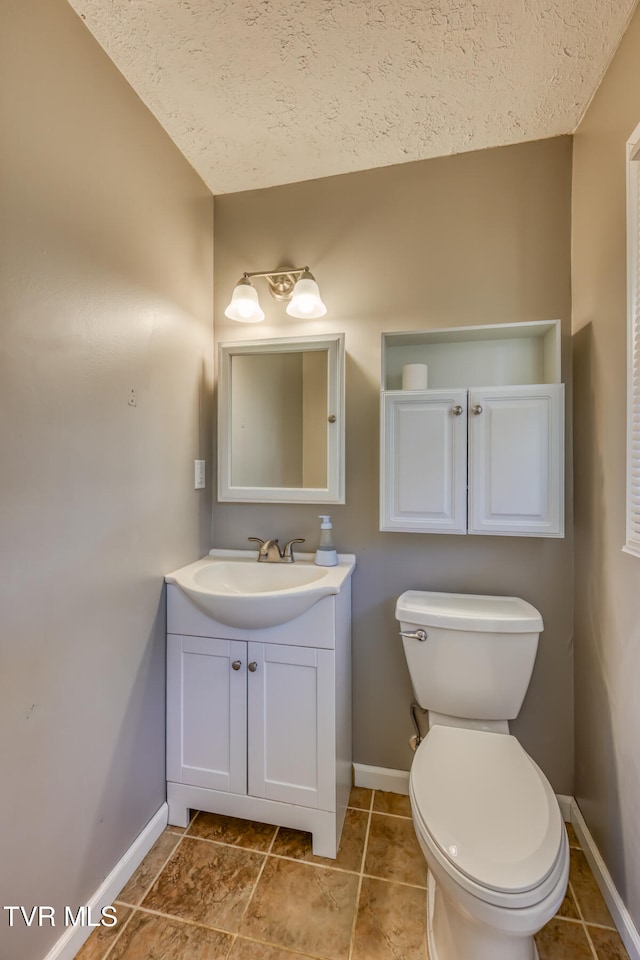 bathroom with toilet, vanity, a textured ceiling, tile patterned flooring, and baseboards