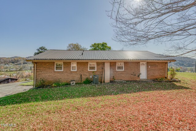 back of property featuring metal roof, central AC, a lawn, and brick siding