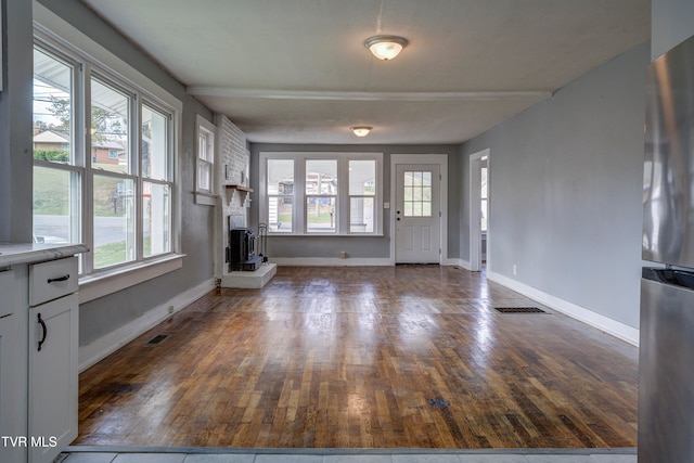 unfurnished living room with a wood stove, a wealth of natural light, and dark hardwood / wood-style flooring