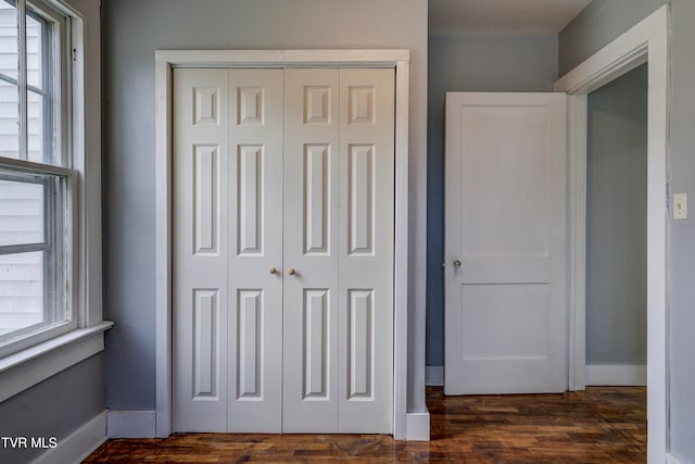 unfurnished bedroom with dark hardwood / wood-style floors, multiple windows, and a closet