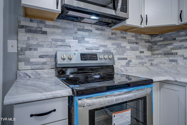 kitchen with tasteful backsplash, white cabinets, light stone counters, and stainless steel appliances