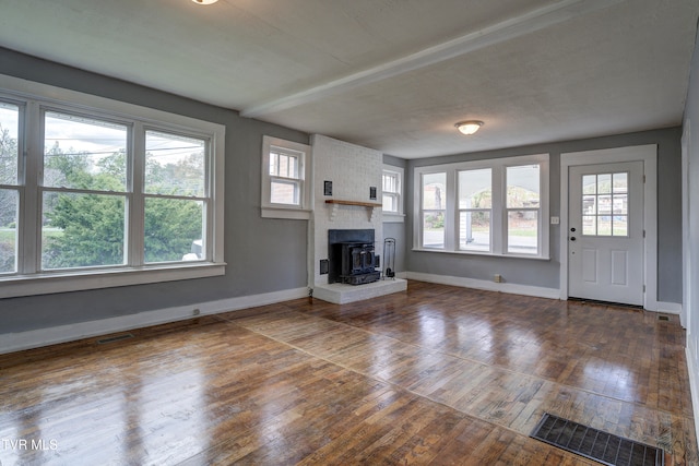 unfurnished living room featuring dark hardwood / wood-style flooring, a wood stove, and a healthy amount of sunlight