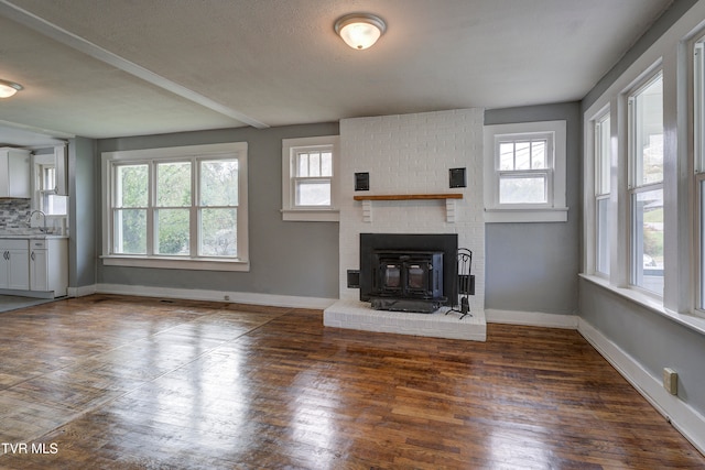 unfurnished living room with a textured ceiling, a wood stove, a healthy amount of sunlight, and dark hardwood / wood-style floors