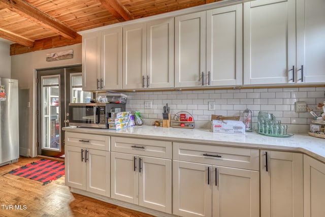 kitchen with light stone counters, stainless steel appliances, light wood-type flooring, white cabinets, and wooden ceiling