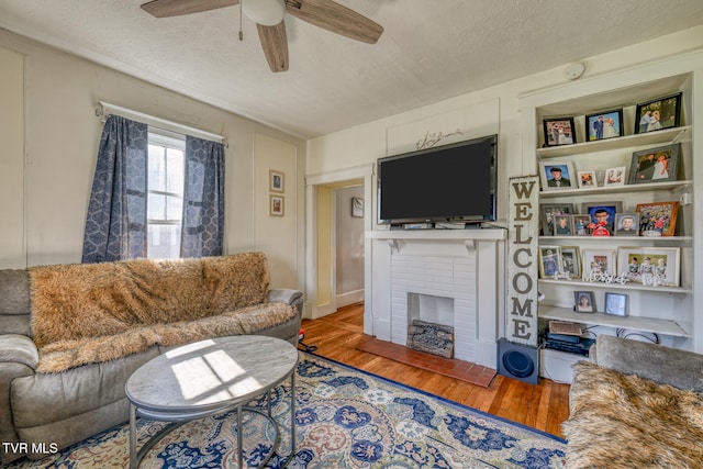 living room featuring a textured ceiling, a fireplace, wood-type flooring, and ceiling fan