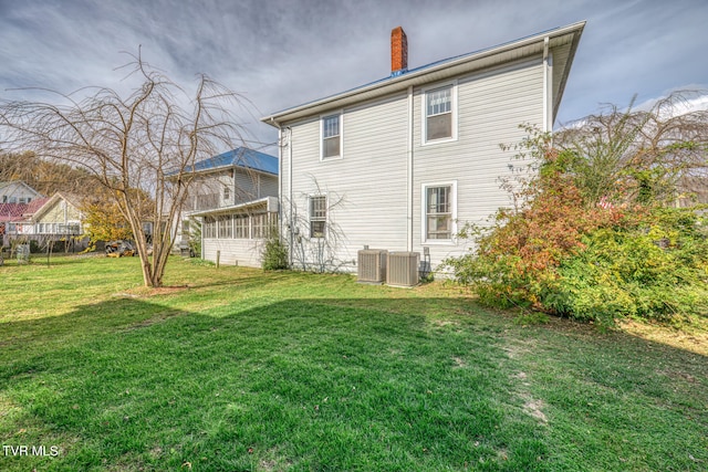 rear view of house with central AC unit, a lawn, and a sunroom