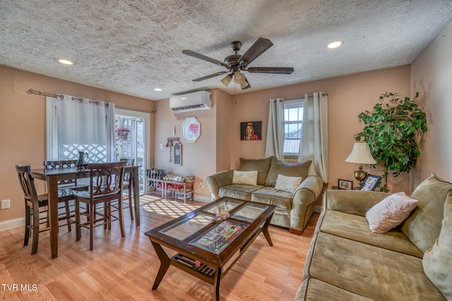 living room with an AC wall unit, light wood-type flooring, a textured ceiling, and ceiling fan