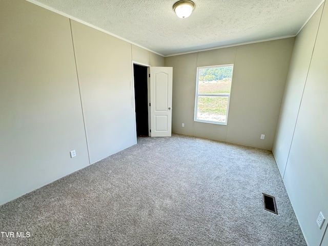 empty room featuring a textured ceiling, carpet flooring, and crown molding