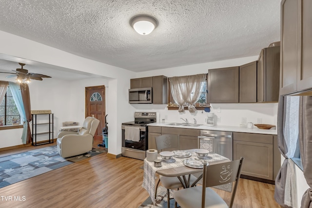 kitchen with stainless steel appliances, light wood-type flooring, a textured ceiling, sink, and ceiling fan