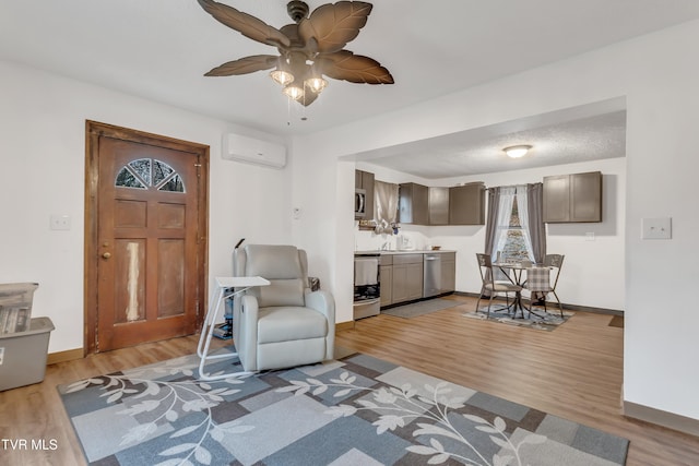 living room with a wall unit AC, ceiling fan, and light hardwood / wood-style flooring