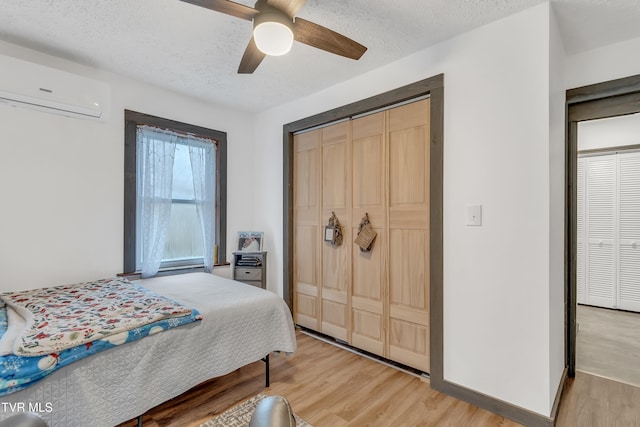 bedroom featuring hardwood / wood-style flooring, a textured ceiling, ceiling fan, and a wall mounted air conditioner