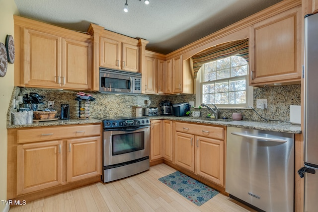 kitchen featuring light hardwood / wood-style floors, stainless steel appliances, a textured ceiling, tasteful backsplash, and light stone countertops