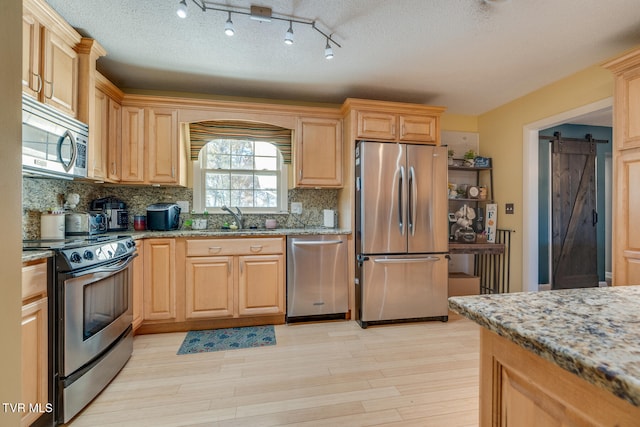 kitchen featuring tasteful backsplash, stainless steel appliances, light wood-type flooring, a textured ceiling, and a barn door