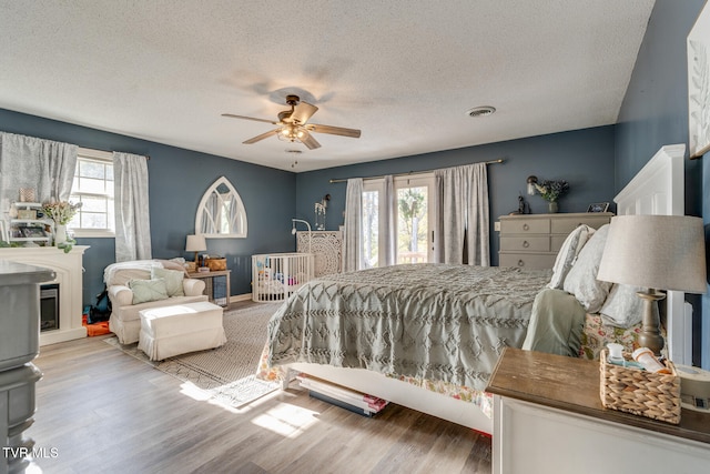 bedroom featuring light hardwood / wood-style floors, ceiling fan, multiple windows, and a textured ceiling