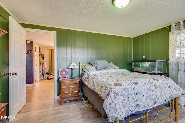 bedroom featuring wood-type flooring, wooden walls, a textured ceiling, and crown molding