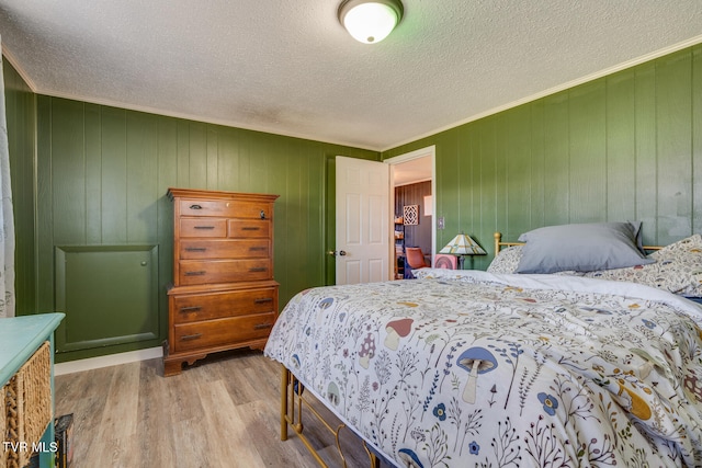 bedroom featuring light wood-type flooring, wooden walls, a textured ceiling, and ornamental molding