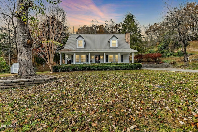 cape cod home featuring covered porch and a storage shed