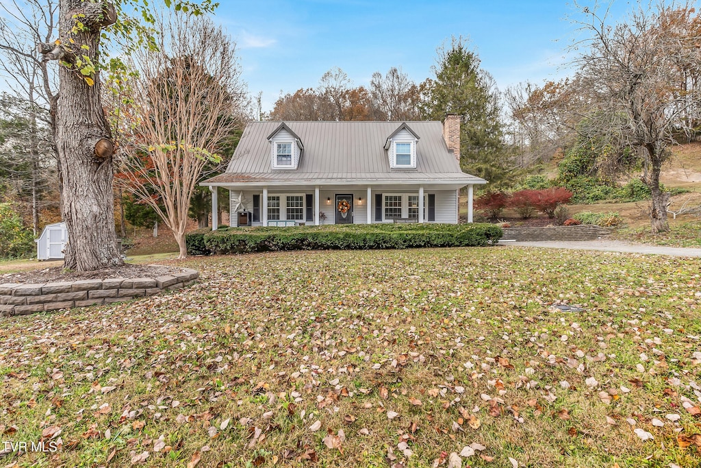 cape cod house featuring covered porch, a front lawn, and a storage unit