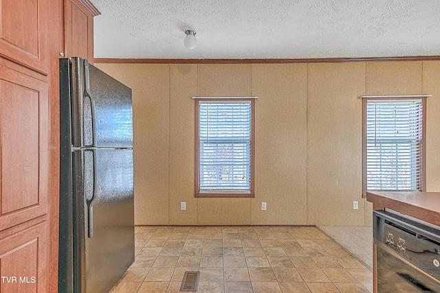 kitchen with black fridge, light tile patterned flooring, ornamental molding, a textured ceiling, and stainless steel dishwasher