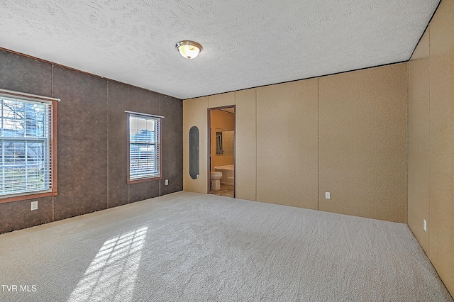 unfurnished bedroom featuring ensuite bath, a textured ceiling, and carpet