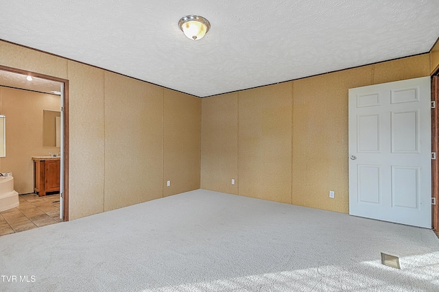 unfurnished bedroom with connected bathroom, a textured ceiling, and light carpet