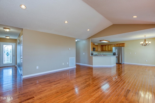 unfurnished living room featuring a textured ceiling, a chandelier, light hardwood / wood-style floors, and vaulted ceiling