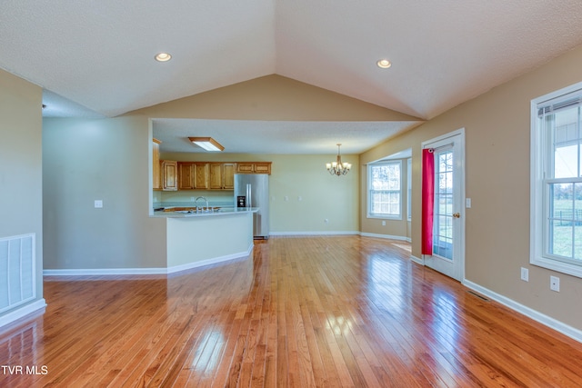 unfurnished living room featuring a textured ceiling, light hardwood / wood-style flooring, a chandelier, and vaulted ceiling