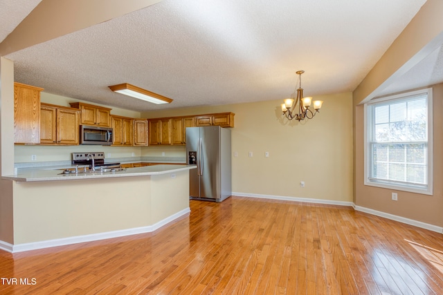 kitchen featuring pendant lighting, appliances with stainless steel finishes, light hardwood / wood-style floors, a textured ceiling, and kitchen peninsula