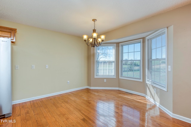 spare room featuring a textured ceiling, light hardwood / wood-style floors, and an inviting chandelier