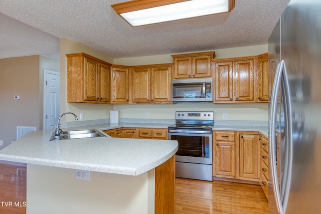 kitchen featuring kitchen peninsula, appliances with stainless steel finishes, a textured ceiling, sink, and light hardwood / wood-style flooring