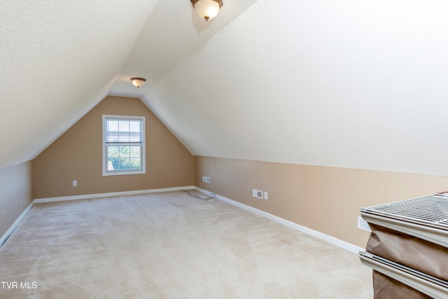 additional living space with a textured ceiling, light colored carpet, and lofted ceiling