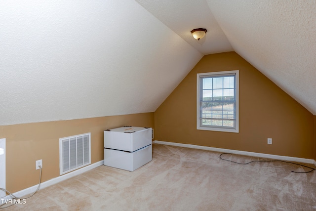 bonus room featuring lofted ceiling, light colored carpet, and a textured ceiling