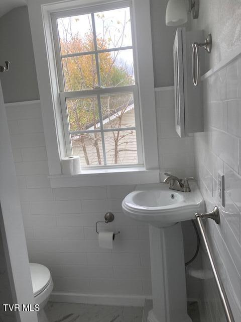 bathroom with toilet and tile walls