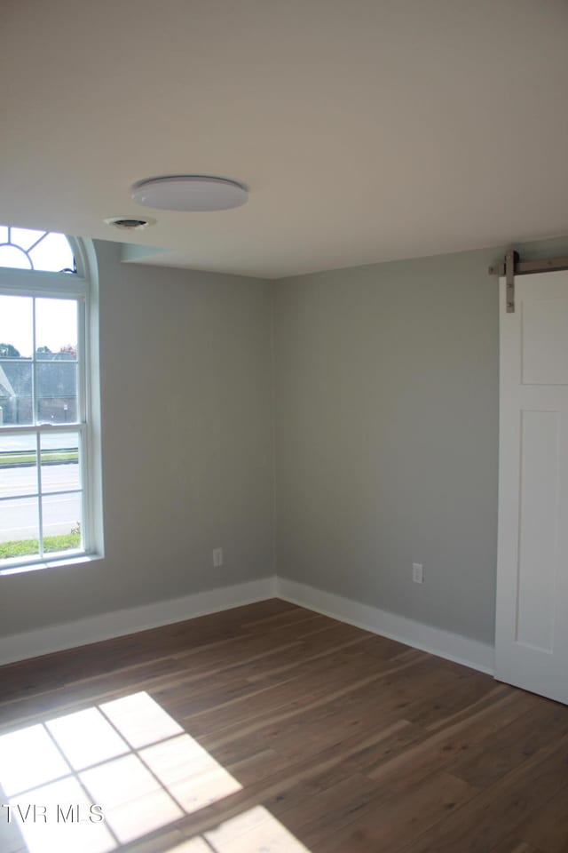 unfurnished room featuring a barn door and dark hardwood / wood-style floors