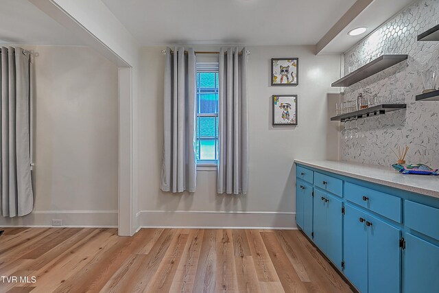 bar featuring blue cabinetry, light hardwood / wood-style floors, and tasteful backsplash