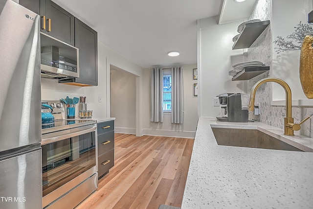 kitchen with sink, stainless steel appliances, light stone counters, decorative backsplash, and light wood-type flooring