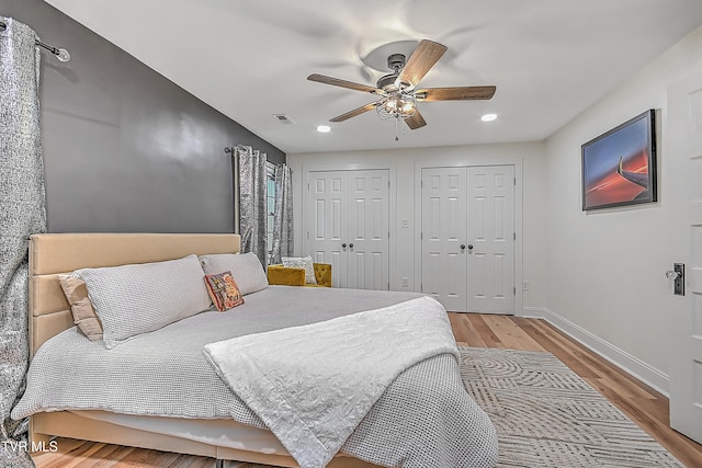 bedroom with ceiling fan, light wood-type flooring, and two closets