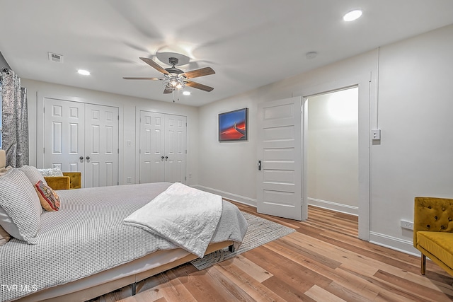 bedroom featuring multiple closets, ceiling fan, and light hardwood / wood-style flooring