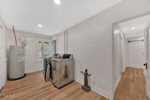 laundry area with washing machine and dryer, water heater, and light hardwood / wood-style flooring