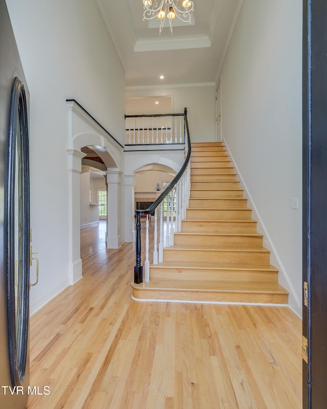 staircase featuring ornamental molding, a notable chandelier, hardwood / wood-style flooring, and decorative columns