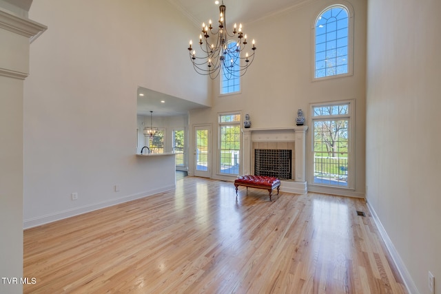 unfurnished living room featuring a high ceiling, light wood-type flooring, an inviting chandelier, and crown molding